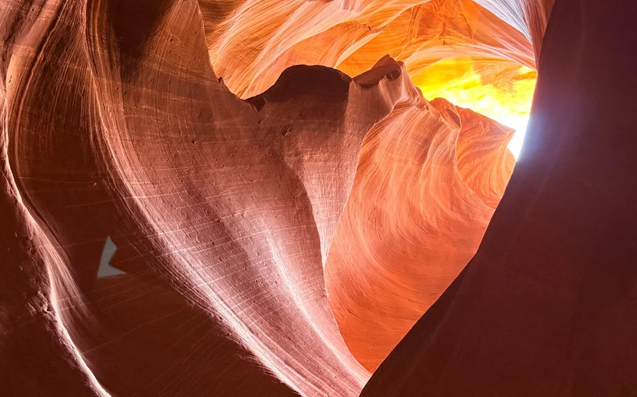 Glatte orangefarbene Canyonwände, die sich um einen hellen Fleck Tageslicht hoch im Slot krümmen