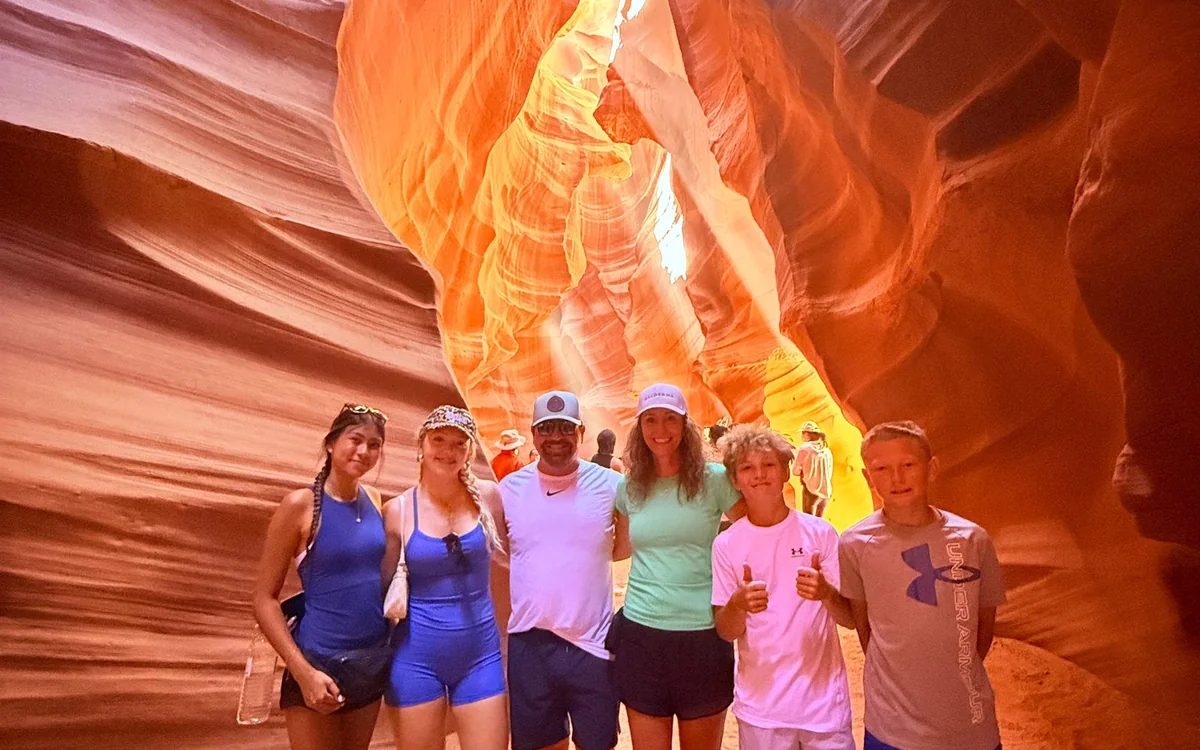 Menschen auf dem sandigen Boden des Canyons, dahinter beleuchtete Sandsteinwände